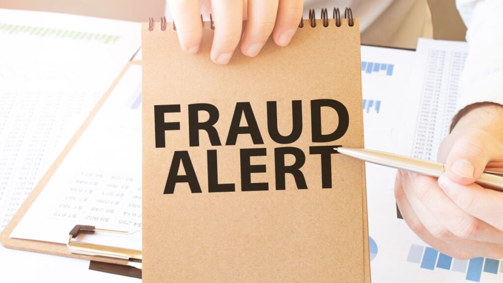 text-fraud-alert-on-brown-paper-notepad-in-businessman-hand