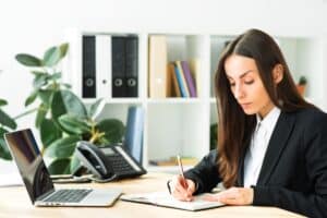 businesswoman-writing-with-pencil-diary-with-laptop-desk